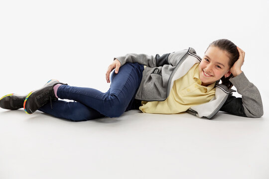 Smiling teenage girl in hoodie and jeans lies on the floor. White background.