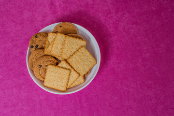 A cookie in a plate is on a pink tablecloth.