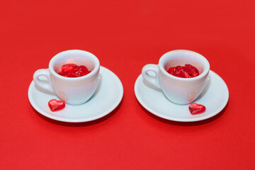two cups with hearts on a red background. the view from the top. red hearts spilled out. isolated on a pink background. copy space