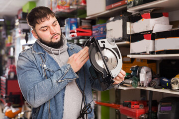 Attentive serious adult male engineer chooses circular saw in tool store