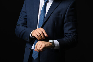 Young businessman with stylish wristwatch on dark background