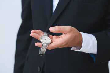 Young businessman holding stylish wristwatch on light background