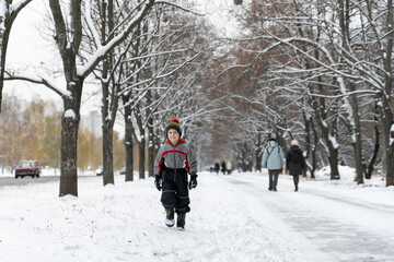 Fototapeta na wymiar Child walks in winter snow-covered park. Little boy on a walk