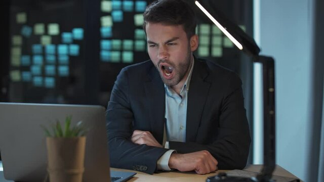 Overworked guy at work, office manager works late, a tired falls asleep in the workplace, night time, man yawns at work.