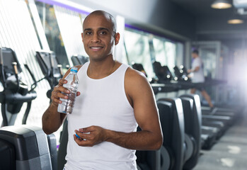 Positive man resting after exercises in fitness gym drinking water