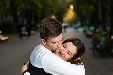 Portrait of beautiful young couple in park. Guy gently kissed the girls cheek