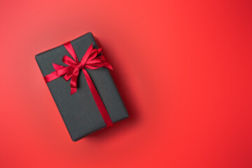 Black gift box with red bow on red background top view, Valentines day, Flat lay style with copy space.