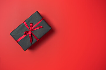 Black gift box with red bow on red background top view, Valentines day, Flat lay style with copy space.