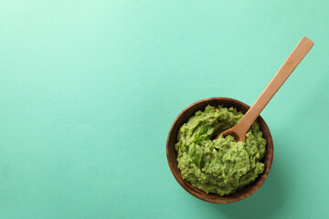 Bowl of guacamole with spoon on mint background, space for text