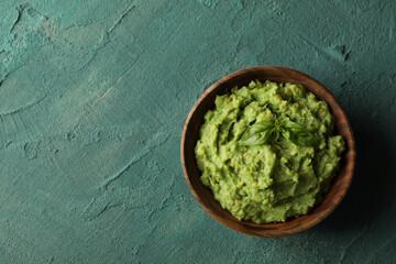 Bowl of guacamole on green textured background, space for text