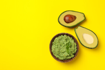 Bowl of guacamole and avocado on yellow background, space for text