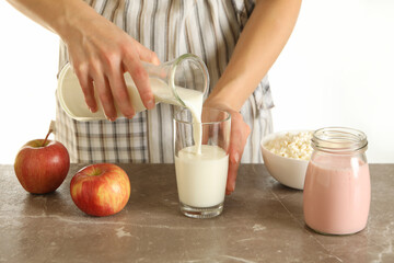 Woman pour milk on gray table with apples, yogurt and cottage cheese