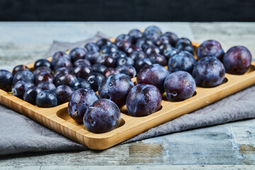 Garden plums on wooden platter with gray tablecloth