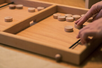 Wooden bard game where you shoot round wooden blocks through opening with help of an elastic band. Two players visible.
