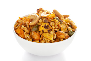 Pile of Indian spicy snacks (Namkeen) - 'All in one' in a white bowl, made with fried peanut, corn flakes, sweet pea, pulses, cashew nuts, etc. side view, against the white background.