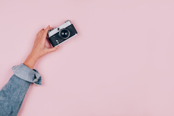 Female hand holding old vintage photo camera on pink background with copy space for text. Trendy...