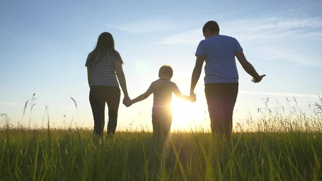 Happy family walks in the park in the sun at sunset. Mom, dad and kid happy walk at sunset in the park. Joint family walks healthy lifestyle. The concept of a happy family and family values