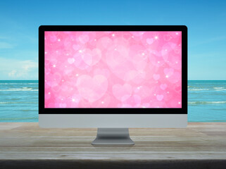 Desktop modern computer monitor with pink love heart screen on wooden table over tropical sea and blue sky with white clouds, Business internet dating online, Valentines day concept