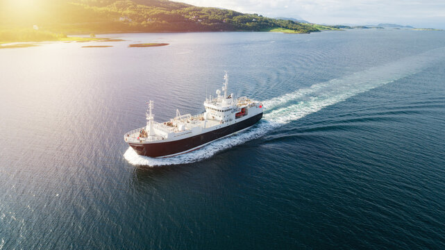 Aerial shot of a cargo ship in the sea. Mountains in the background, Norway, Lofoten.