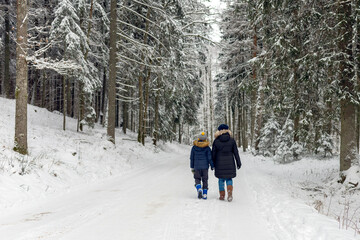 Mother and son walking together on a forest track in winter time.