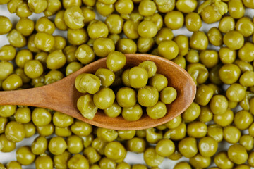 A heap of boiled green peas with a wooden spoon on a white table