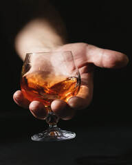 Cognac glass in man's hand. Bright amber drink. Dark background