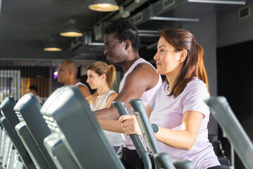 Young adult woman doing cardio workout using elliptical cross trainer at fitness center