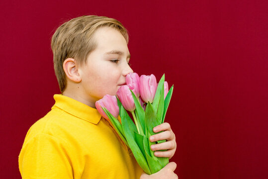 A happy son boy kid snuff tulips on red studio background.Side view image.