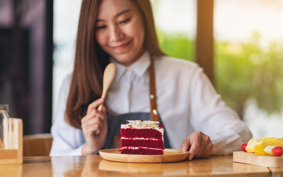 Closeup image of a beautiful woman, female chef baking and eating a piece of red velvet cake in wooden tray