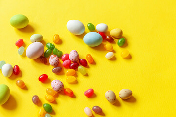 Happy Easter concept. Preparation for holiday. Easter candy chocolate eggs and jellybean sweets isolated on trendy yellow background. Simple minimalism flat lay top view copy space.