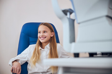 Pretty cute child sitting on the medicine chair in ophthalmologist cabinet