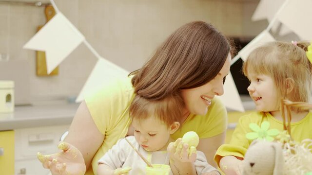 Happy easter. A mom and her two baby girls painting Easter eggs at domestic kitchen