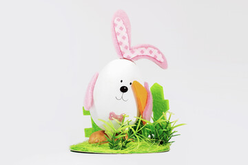 Easter egg with ears in the form of an Easter bunny, with carrots on a green lawn. Easter card. Minimal easter concept