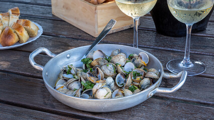Recipe for cockles with garlic and parsley in an aluminium casserole dish, accompanied by a champagne drink