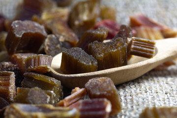 Dried rhubarb candied fruits in a wooden spoon. Candied rhubarb on a canvas fabric background. Dry rhubarb close - up macro photography. Rheum.