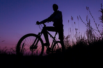 Silhouette of a cyclist against sunrise sunset pink blue violet sky