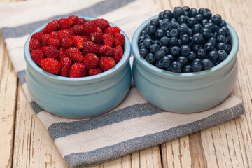 Organic berries bilberry and strawberry in blue bowls on wooden background, healthy eating concept
