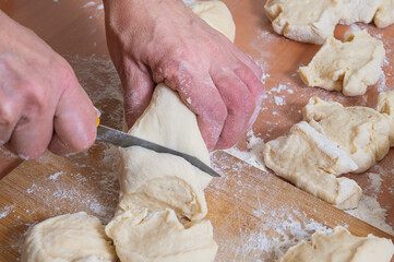 A woman cuts the finished dough into pieces for patties with a knife. Women's hobby. Homemade baking