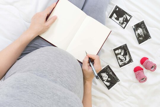 Pregnancy dairy.Top view of pregnant woman writing thoughts down in notebook for memory,x-ray image of her baby  and shoes.Concept of pregnancy, Maternity prenatal care. Mom with a new life