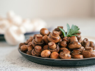 Ready-to-eat fried mini champignons on plate with copy space. Perfect mini mushrooms heap on plate over gray cement background. Natural day light