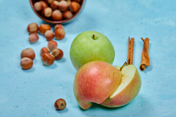Apples, cinnamon and bowl of hazelnuts on blue background