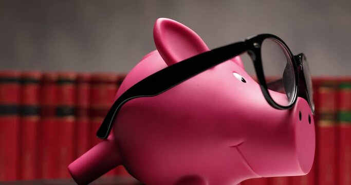 piggy bank moving from side to camera and wearing glasses against a row of books 