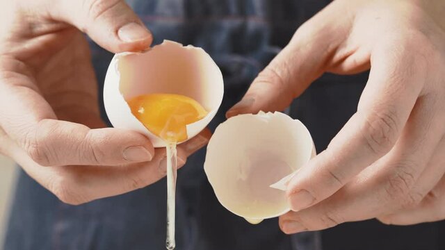 Women's hands separate the yolk from the white in a broken egg.