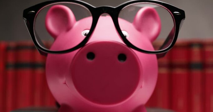 nerd piggy bank sliding from right to left and wearing glasses in front of books 