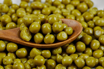 A heap of boiled green peas with a wooden spoon on a white table