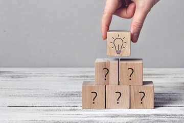 Wooden cubes with drawings of questions and a burning light bulb. A symbol of difficult questions...