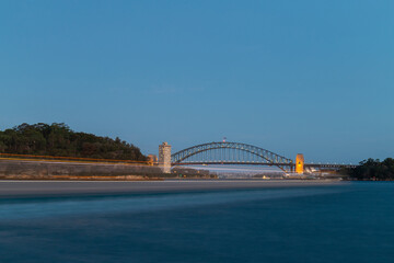 Obraz premium Boat travelling in front of Sydney Harbour Bridge at dusk.