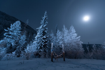 Night view of the Yakut landscape with a moonlit halo and wooden pillars - serge for coaxing the spirits for the good luck of travelers. Winter Forest at night