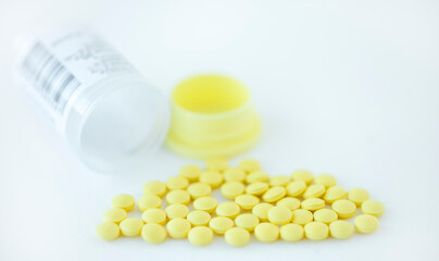 Yellow pills and empty bottle on light background