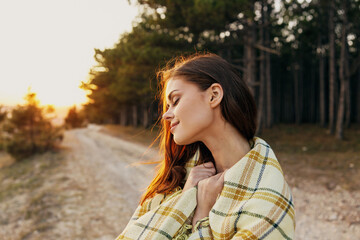 Naklejka premium Beautiful woman with a plaid on her shoulders at sunset is resting in the forest park